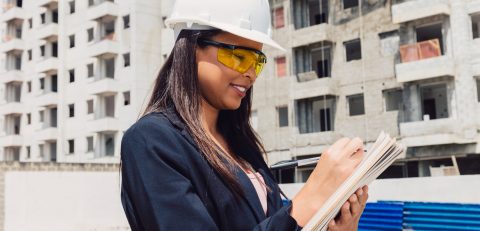 african-american-lady-safety-helmet-with-notepad-near-building-construction